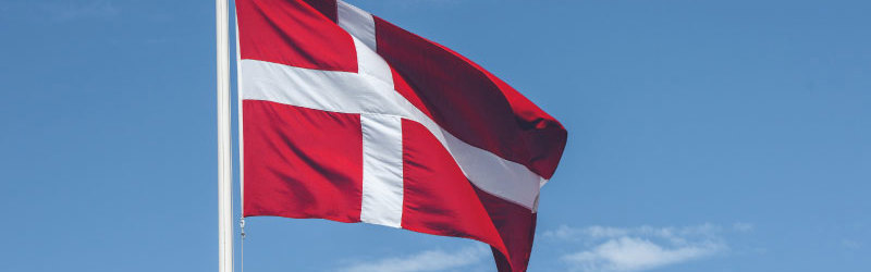 Dannebrog til tops i flagstang med blå himmel som baggrund